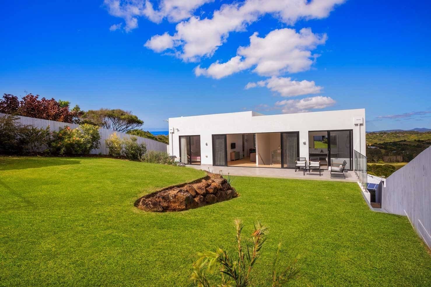 Rear exterior of a white modern home with large sliding glass doors opening onto a flat, grassy lawn.