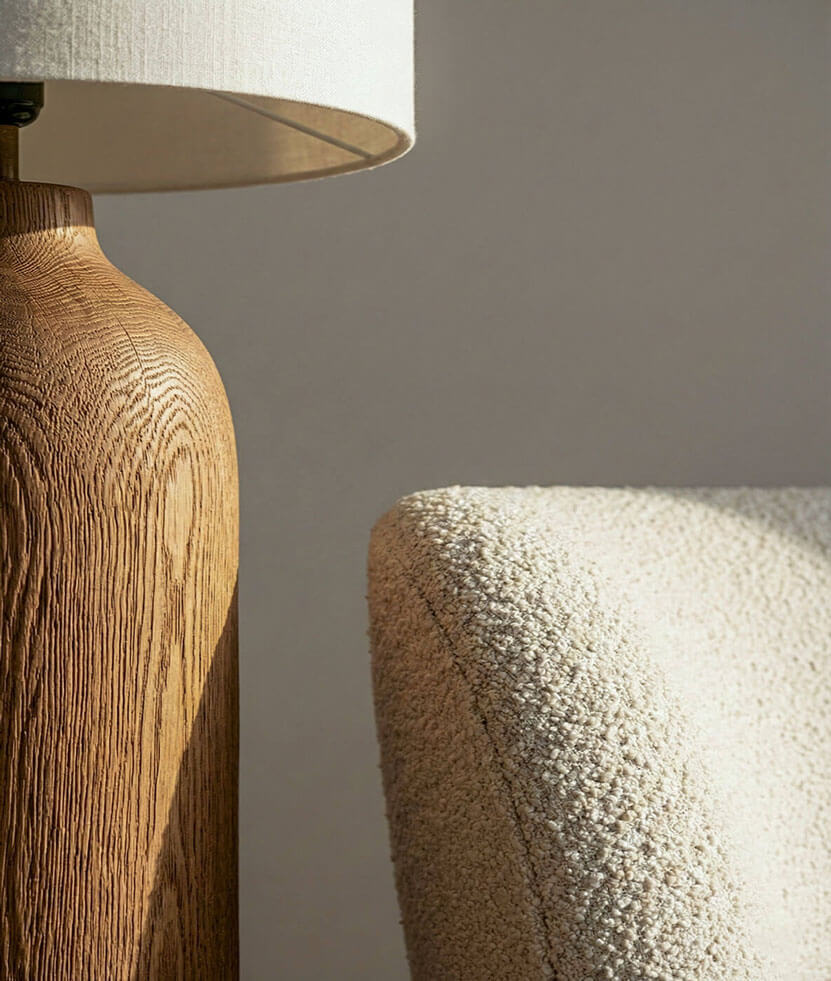 A macro photography shot showing the detailed grain of a custom-milled timber lamp base positioned against woven upholstery.