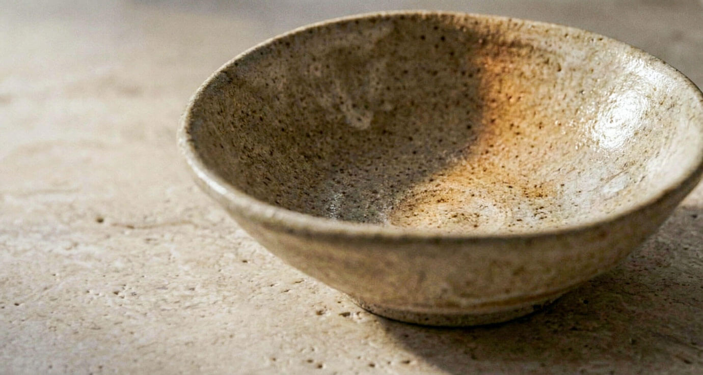 A close-up detail of a hand-thrown ceramic bowl with visible throwing rings and an organic glaze, resting on a natural stone surface.