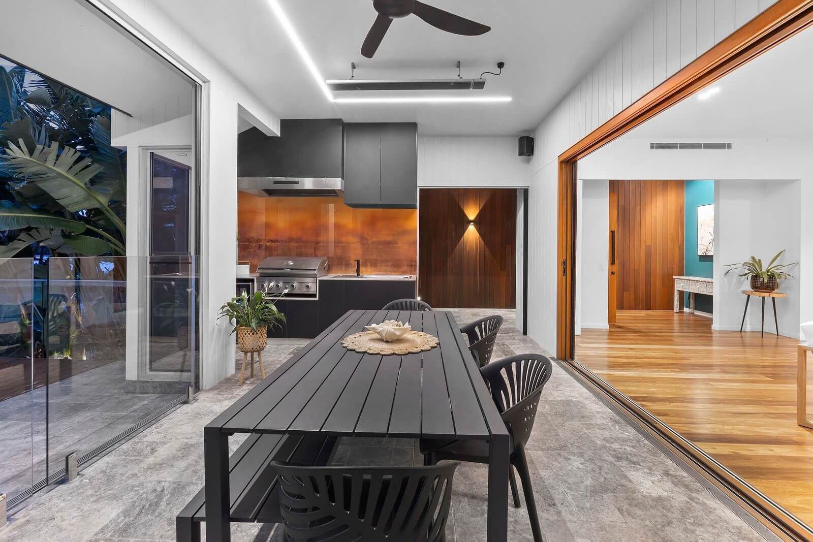 Covered outdoor entertaining area with dining table, showing external stairs connecting the upper level to the pool deck.