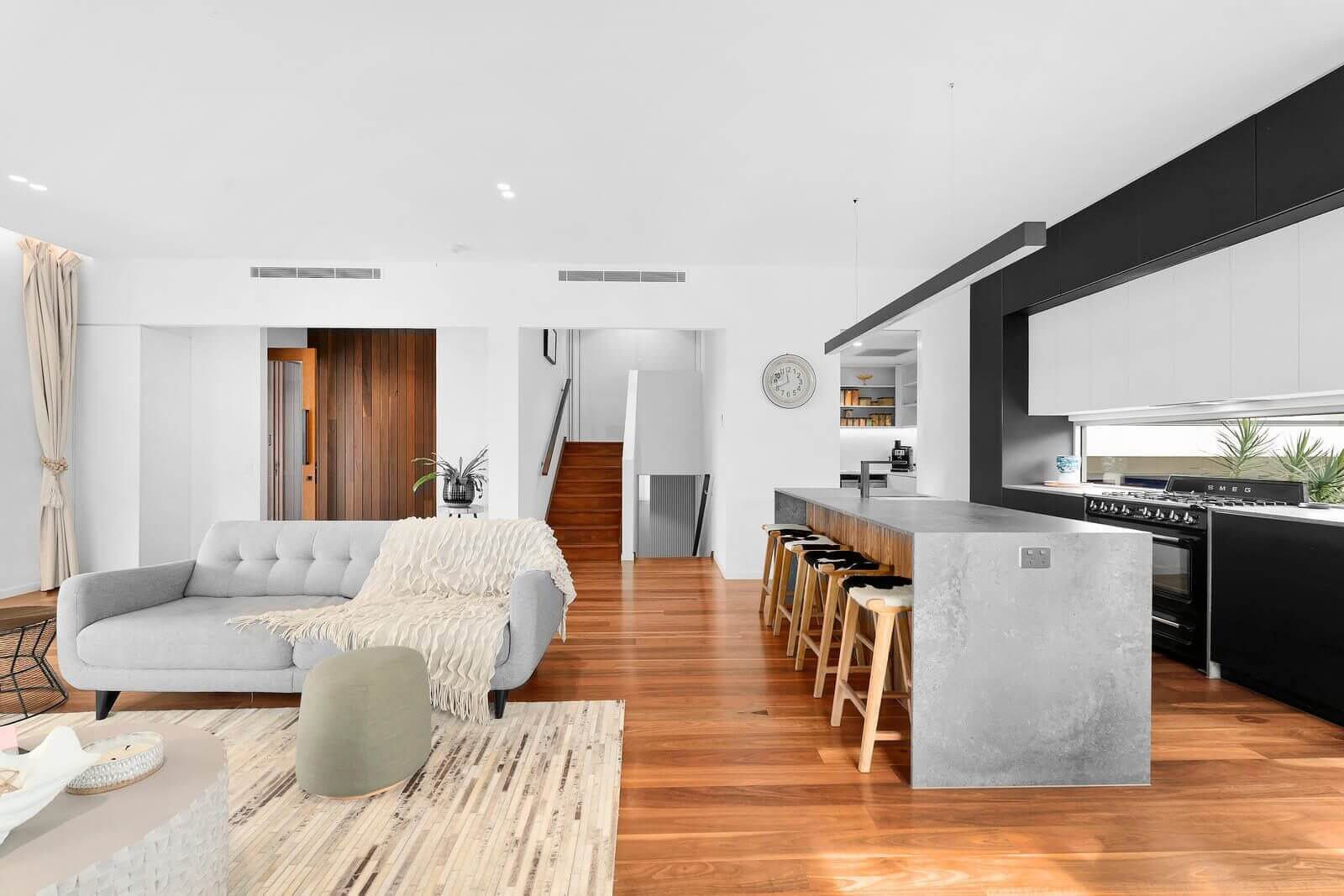 Open plan living and kitchen area with polished timber floors, looking towards a staircase and hallway.
