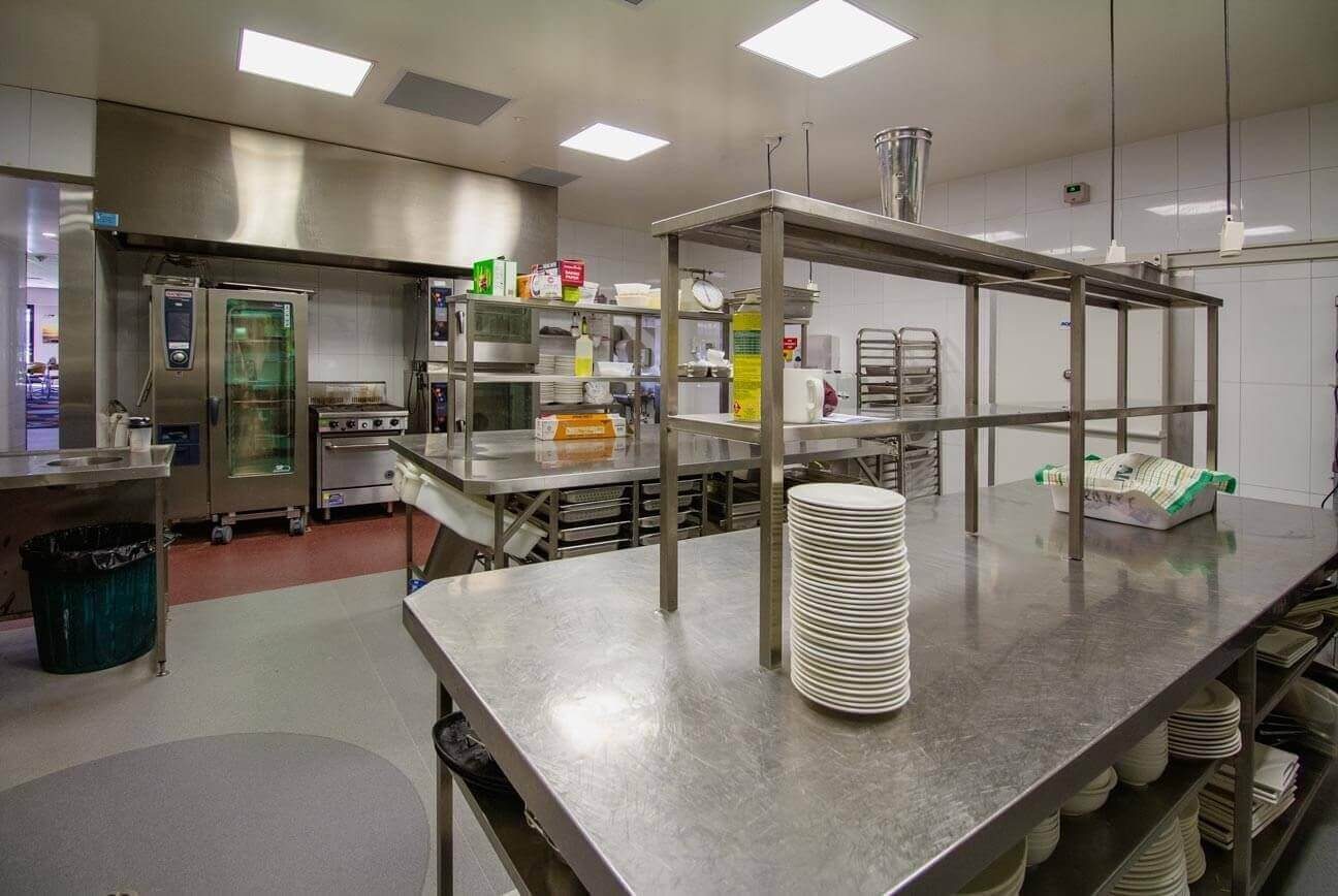 A professional cooking line with industrial ovens, stainless steel work surfaces, and stacks of white plates.