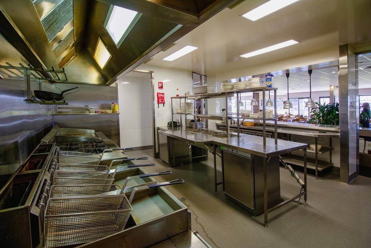 Detailed view of heavy-duty deep fryers and stainless steel splashbacks leading toward a brightly lit service window.