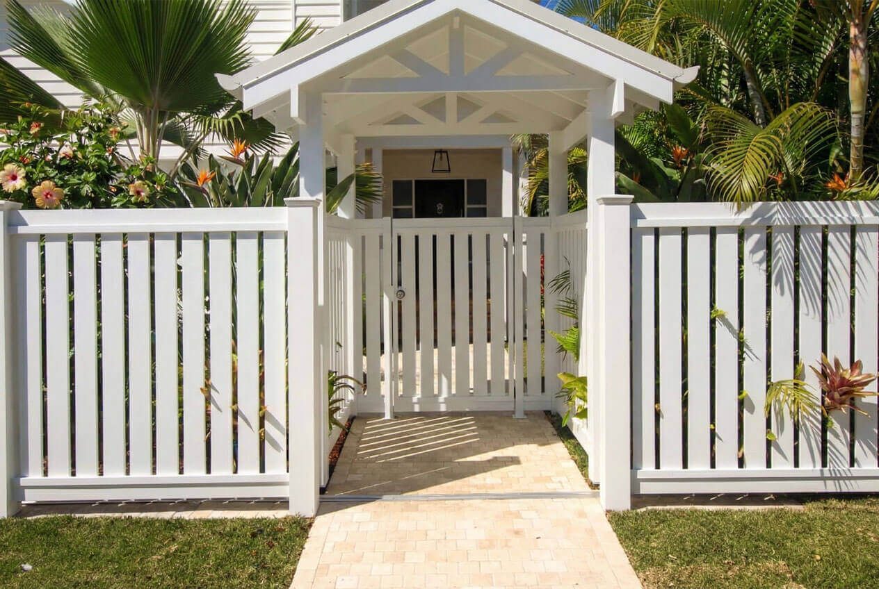 White timber gatehouse with gable roof, picket fence and tropical landscaping.