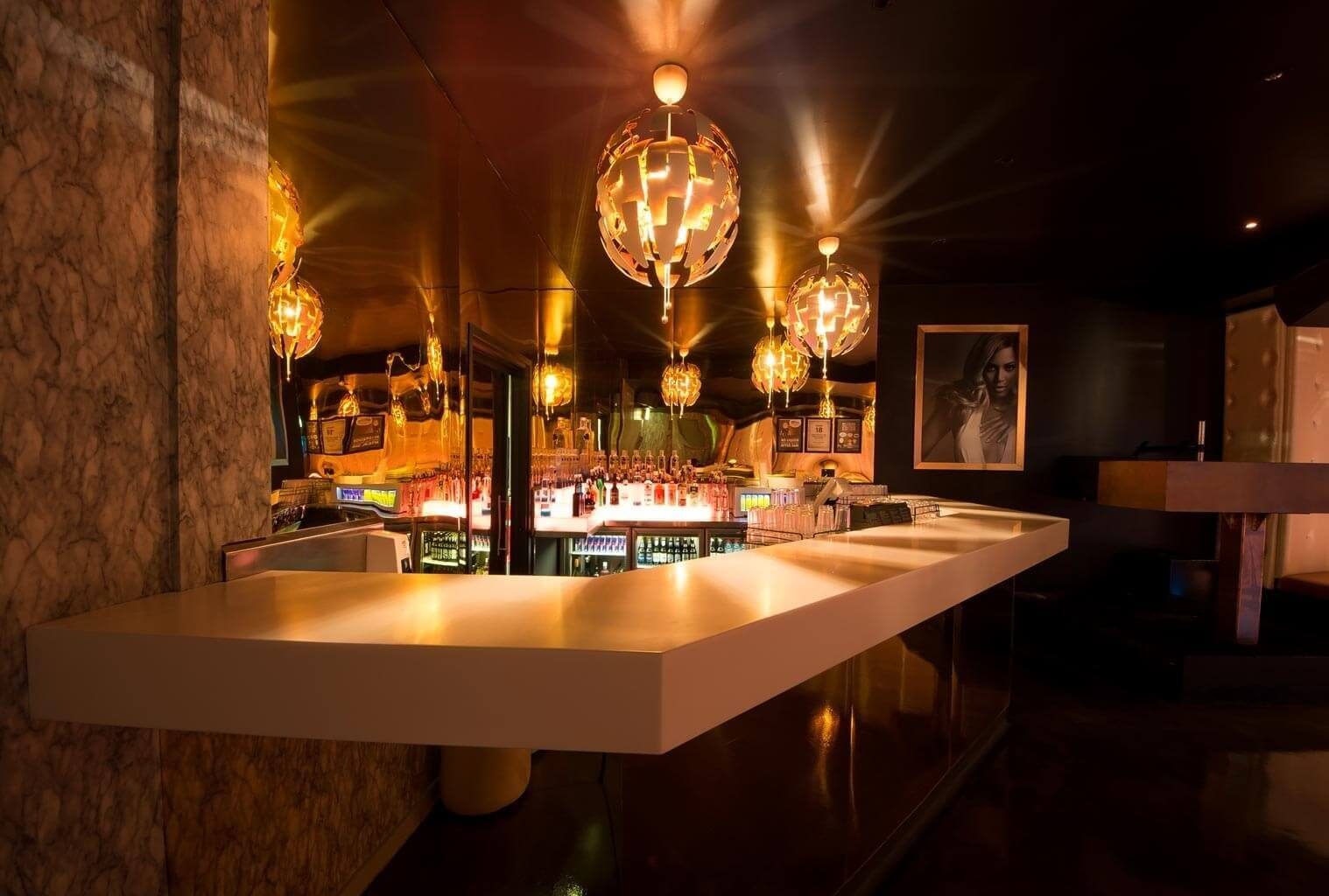 Bar service area featuring warm lighting, reflective surfaces, and suspended metallic pendant lights.