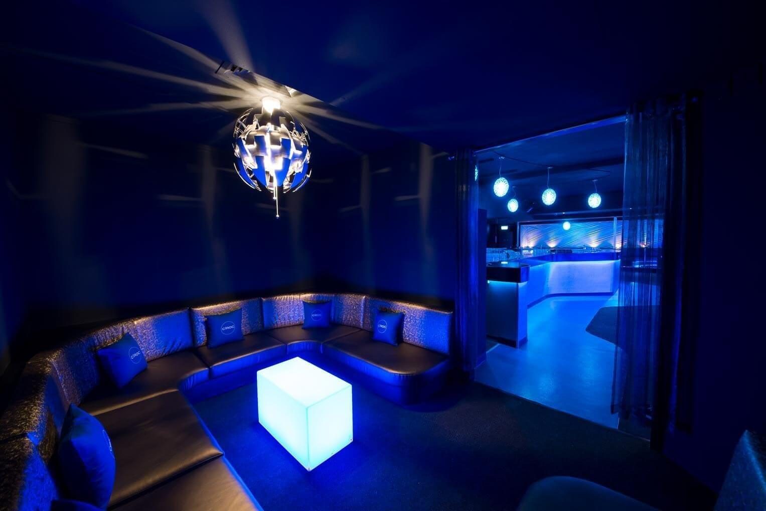 Private seating enclave with custom upholstery, glowing cube tables, and deep blue ambient lighting.