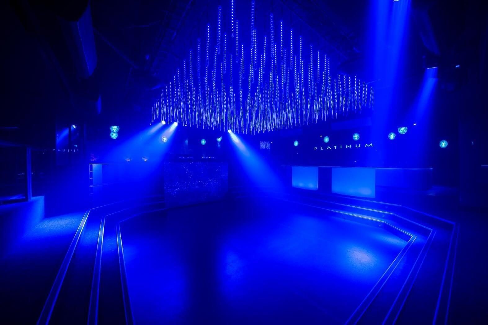Sunken central dance floor illuminated by an overhead LED matrix, featuring a stepped perimeter and an elevated DJ booth.