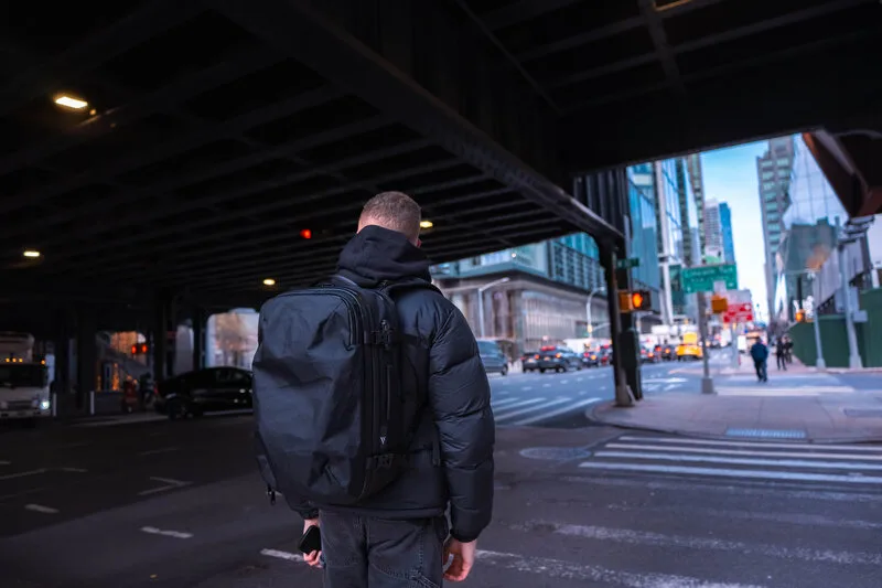 Traveler carrying the Zephyr Pro beneath an elevated trestle toward a sunlit New York street