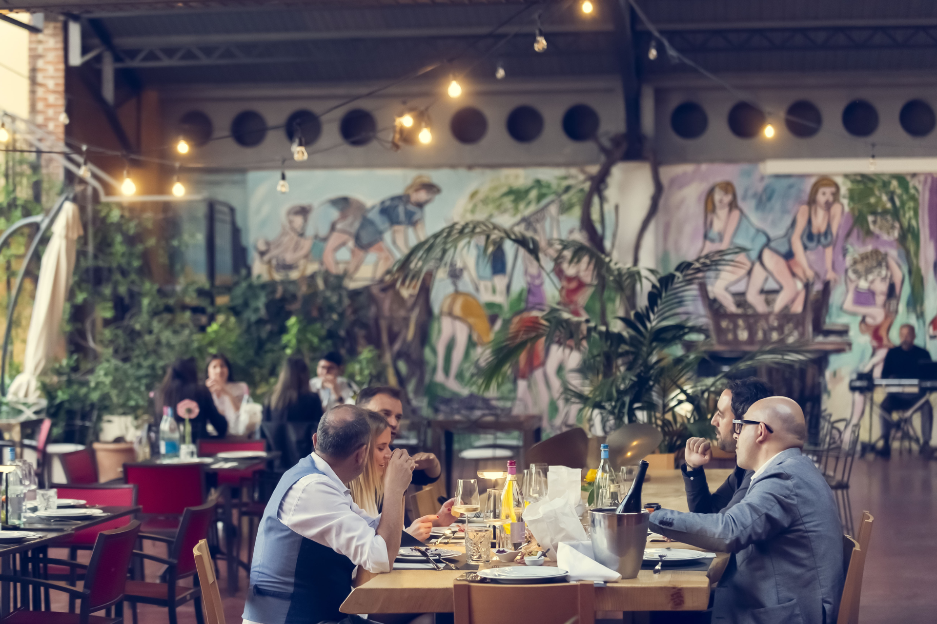 Persone che cenano in un ristorante con un murale sullo sfondo.