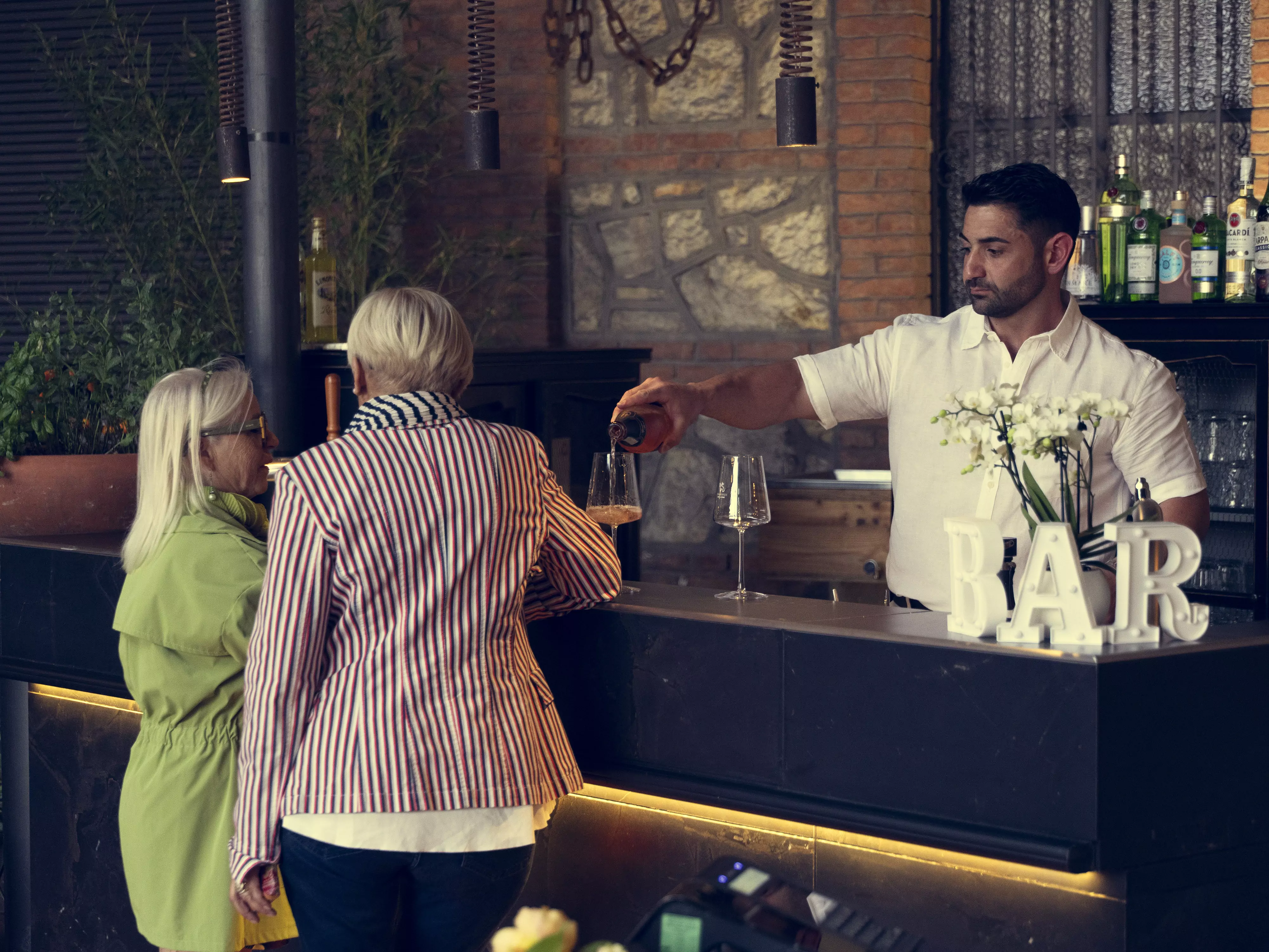 Un barista serve bevande a due donne anziane in un bar.