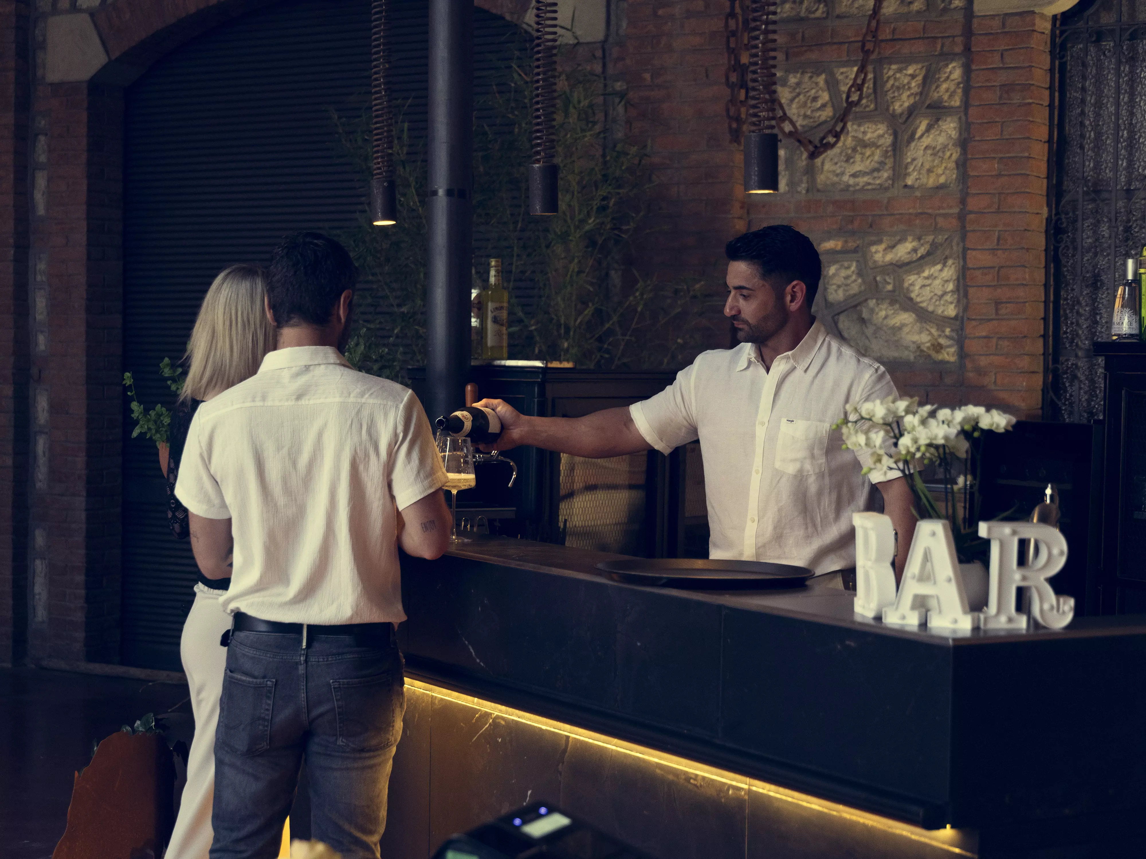 Un barman serve bevande a una coppia in un bar.