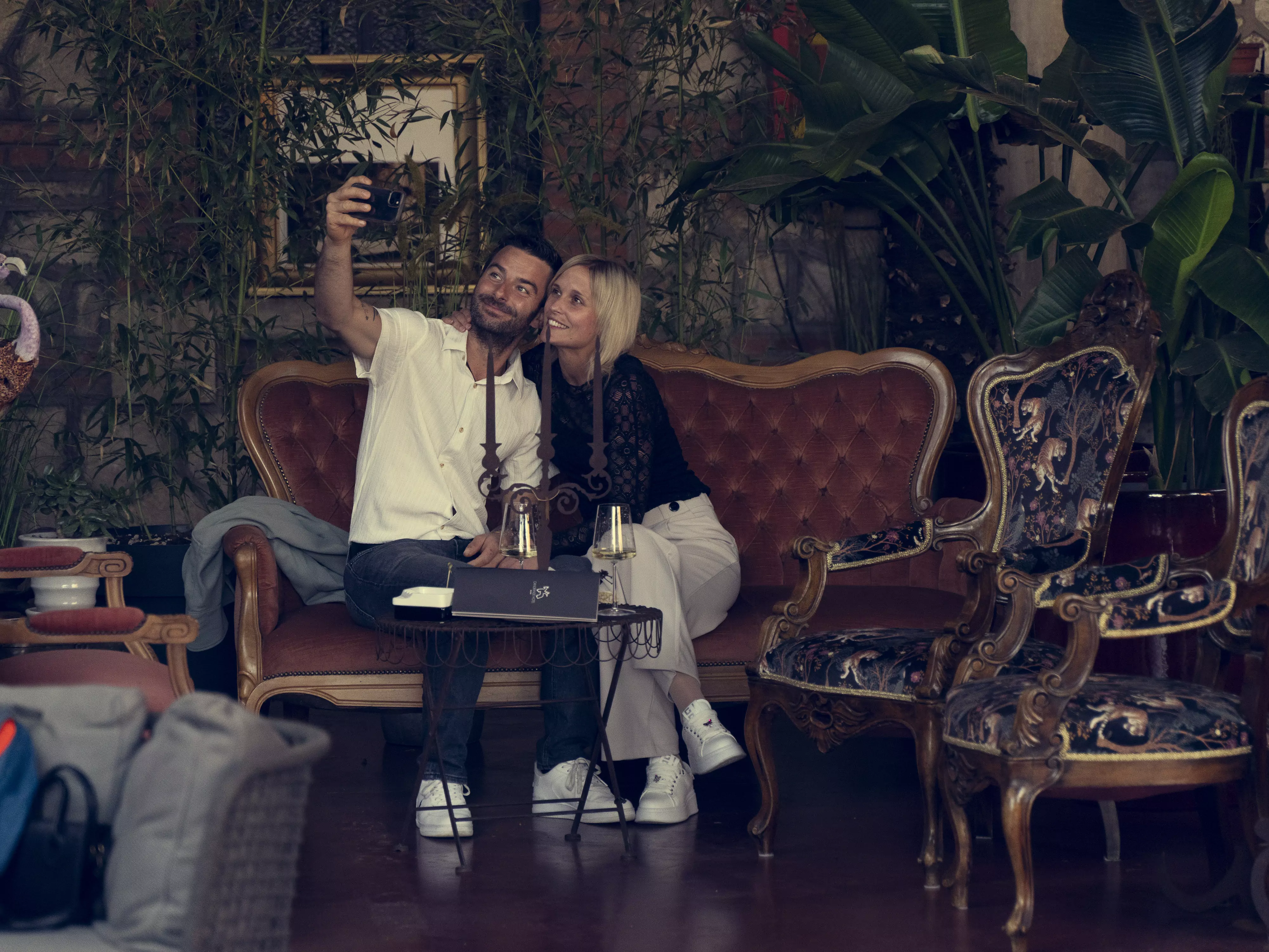 Una coppia si scatta un selfie seduta su un divano dall'aspetto elegante in un ristorante.