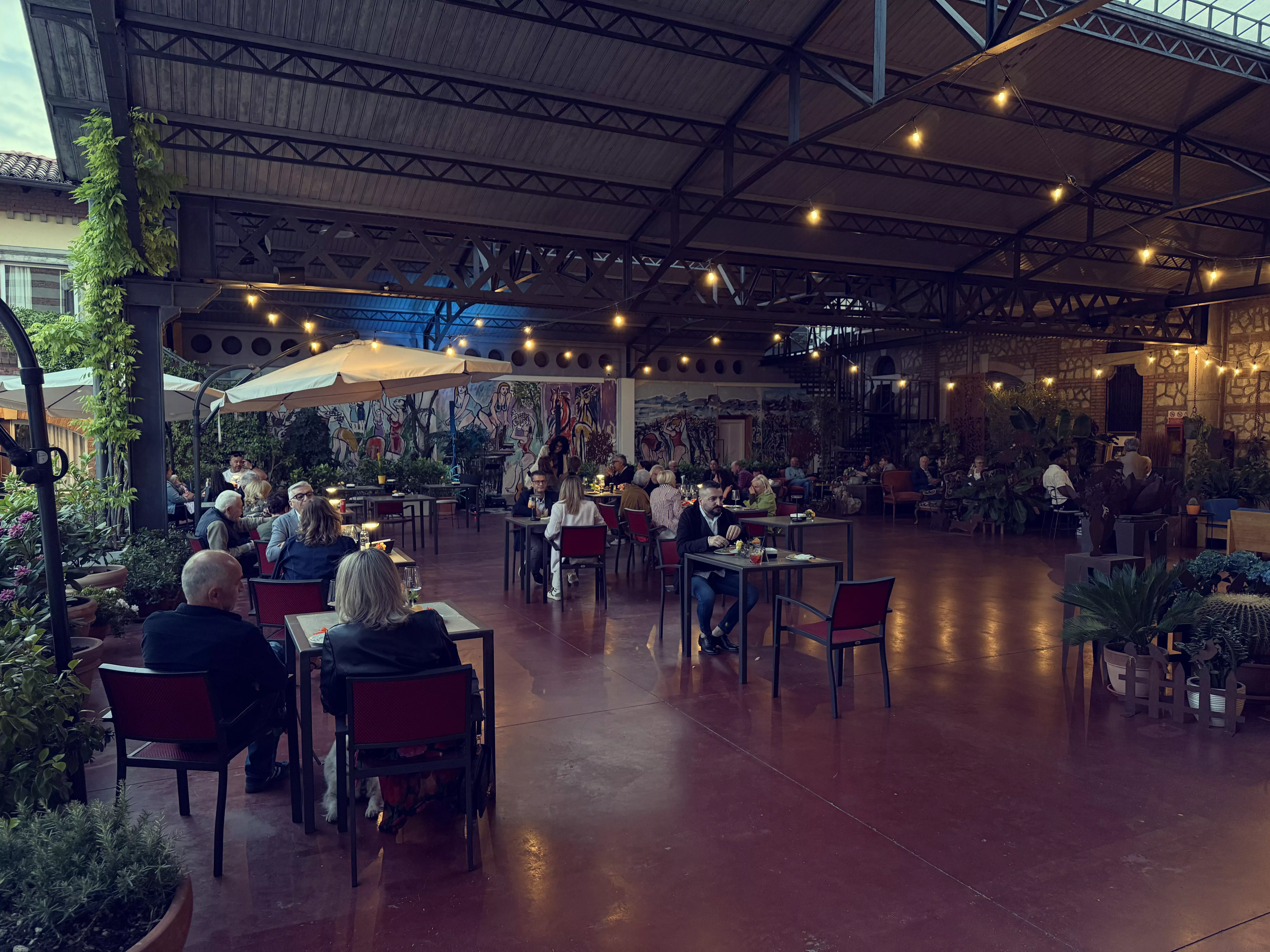 Clienti seduti ai tavoli di un ristorante all'aperto sotto luci brillanti.