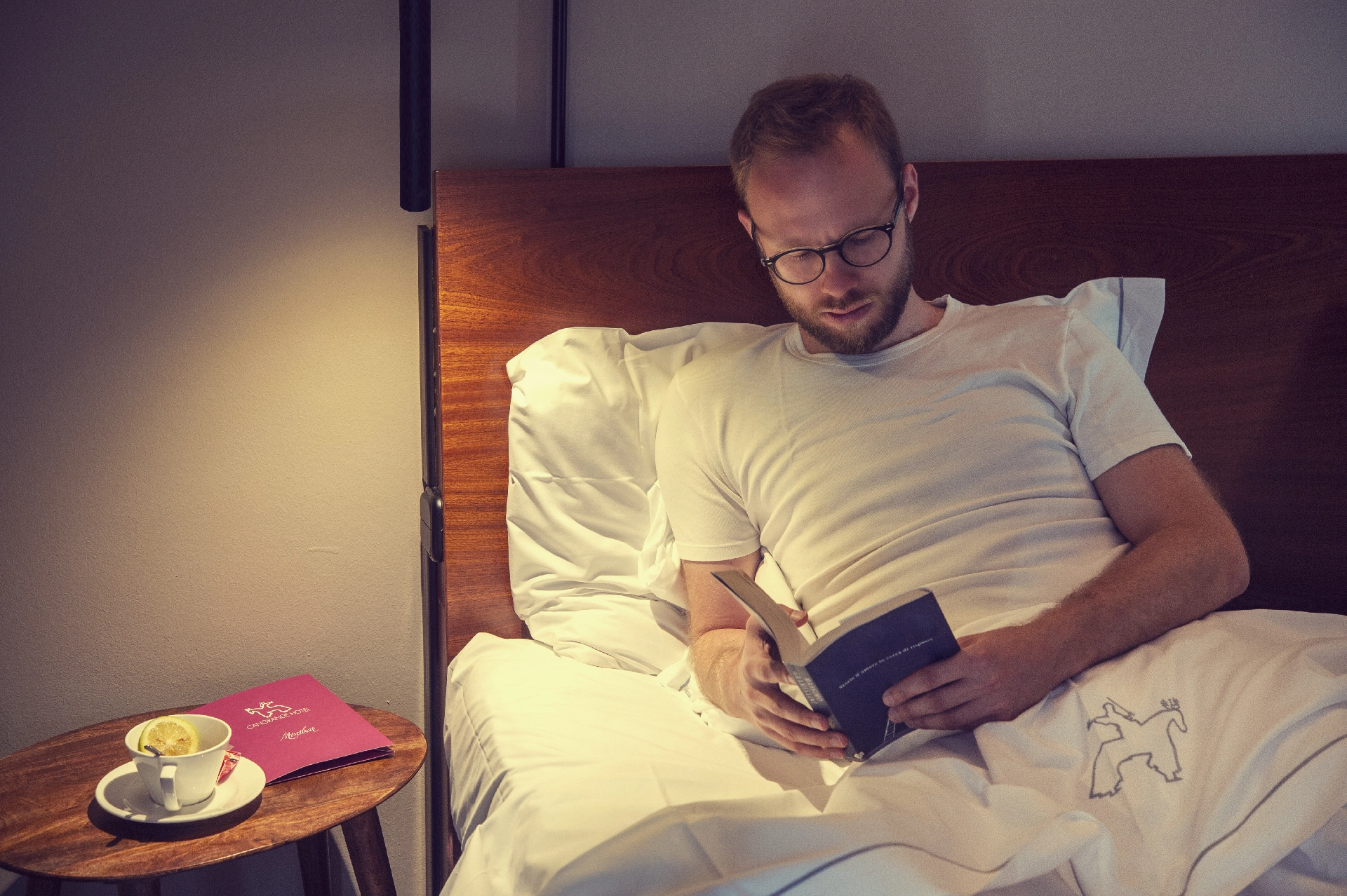 Uomo che legge a letto con una tazza di tè sul comodino.