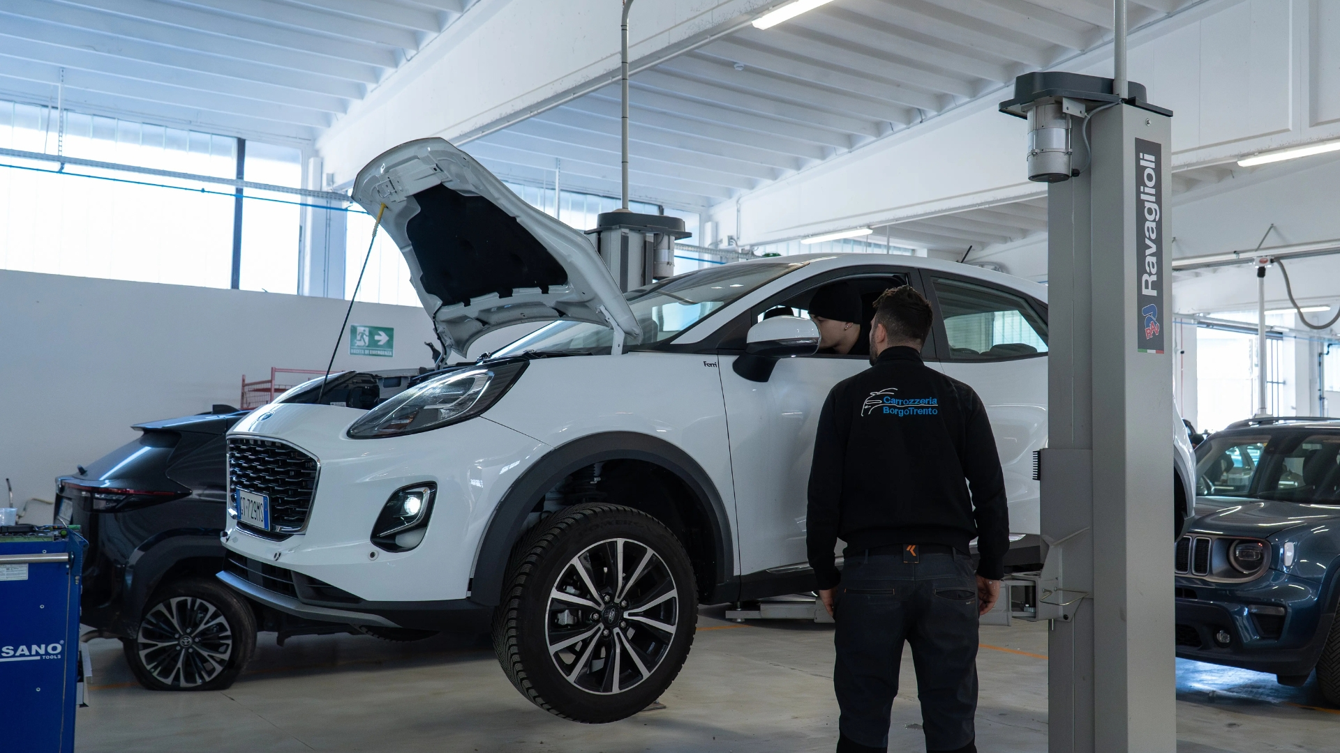In officina carrozzeria borgotrento, auto bianca è sollevata per la manutenzione da parte dei dipendenti.