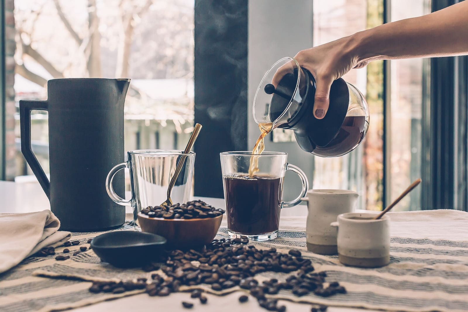 Fresh brewed coffee poured at a window table, roasted beans scattered around