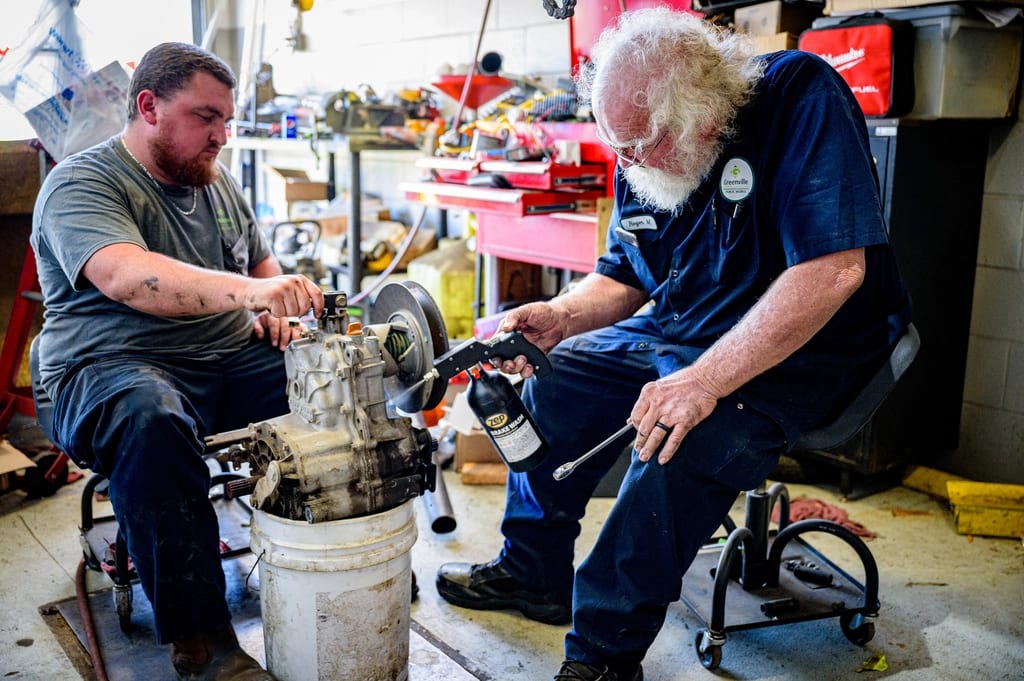 Two mechanics servicing a part together in the workshop