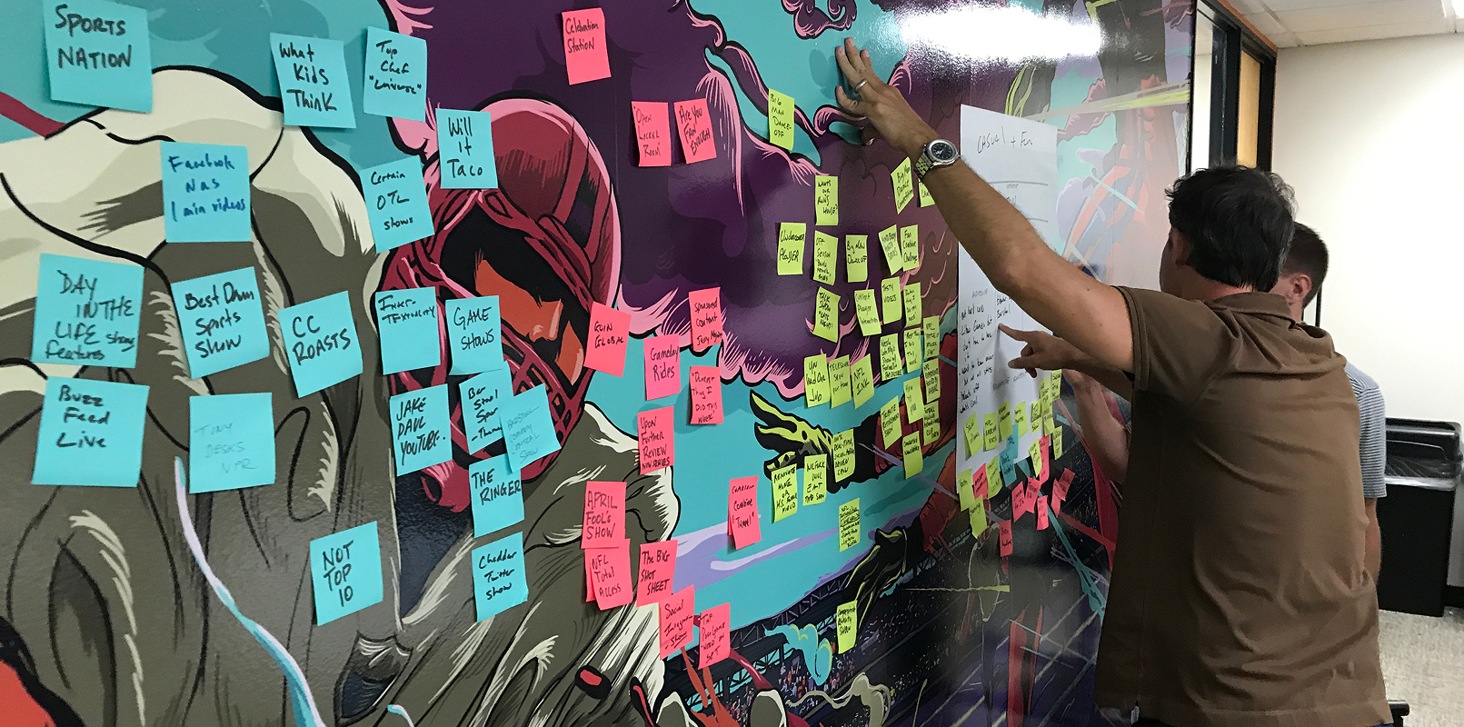 Participant adds notes to a dense content-strategy map filled with pink, blue, and green ideas.