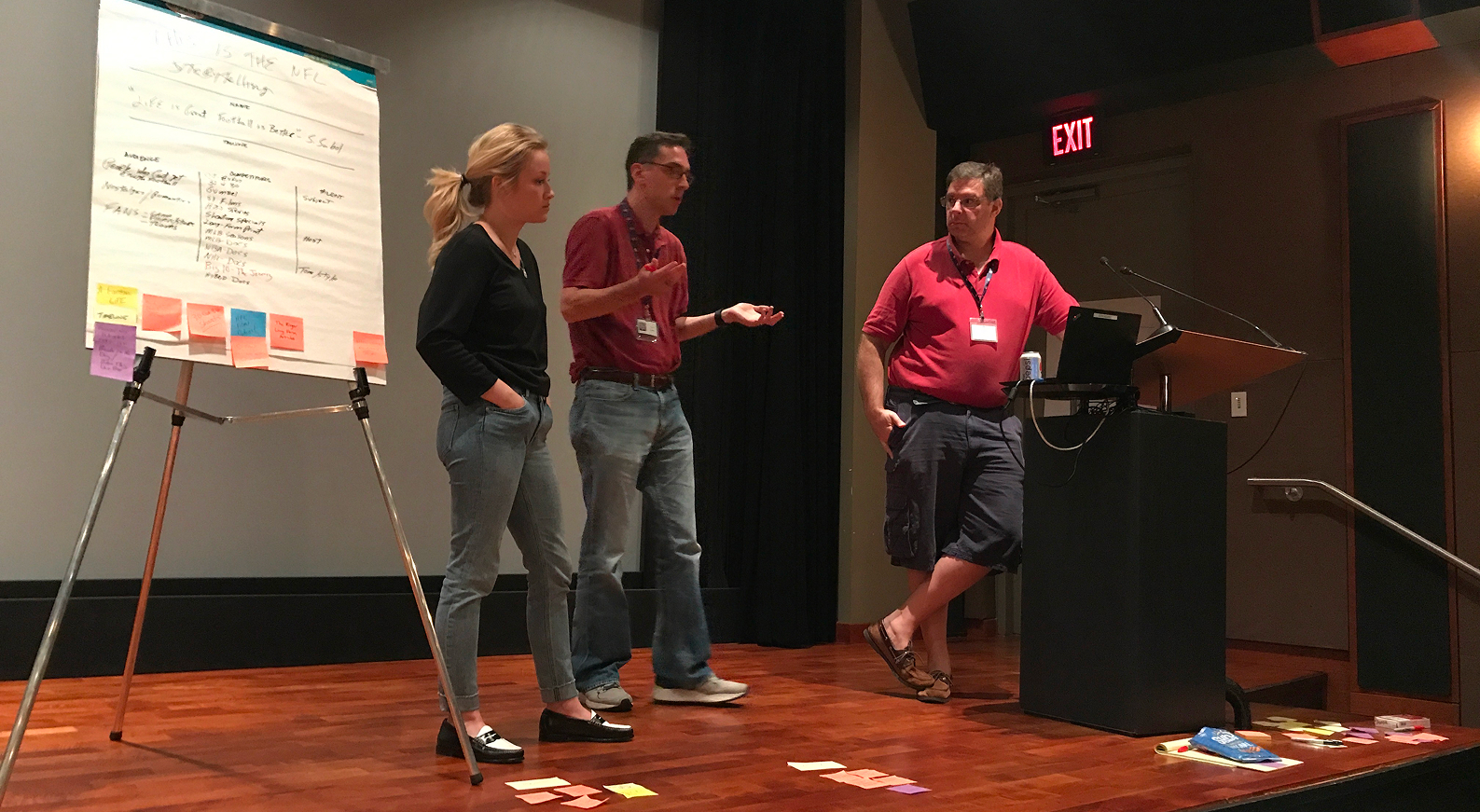 Three facilitators present beside a large workshop chart at the front of the room.
