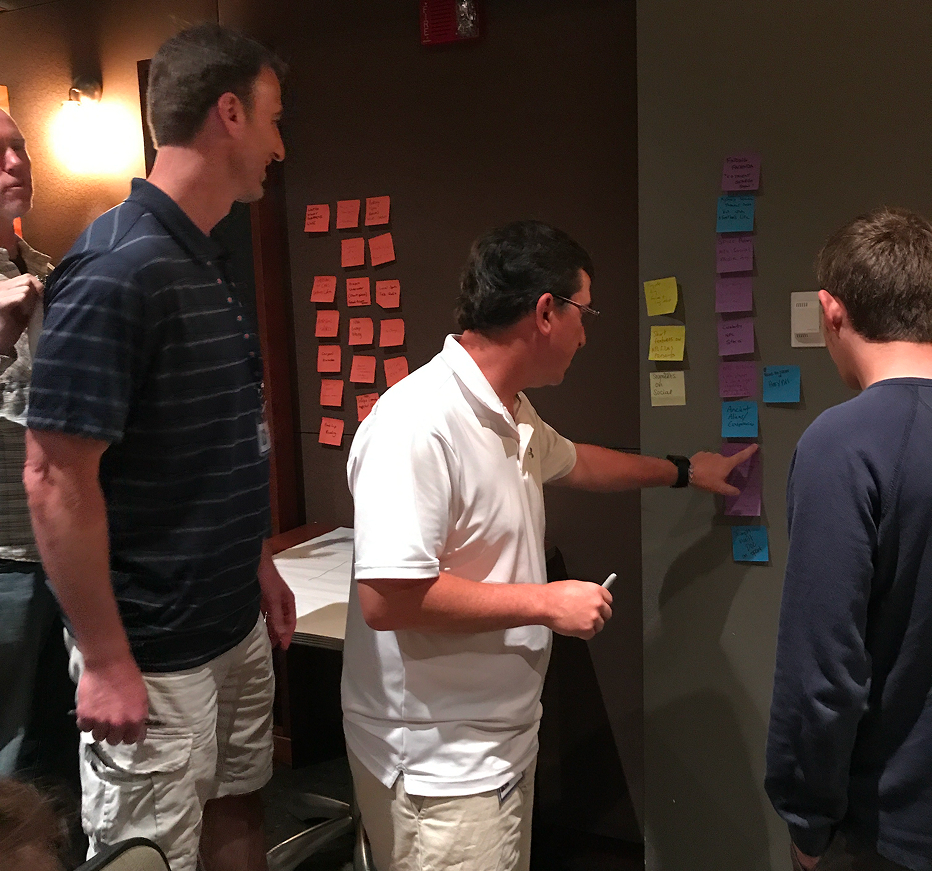 Participants cluster color-coded sticky notes on a wall during an affinity-mapping exercise.