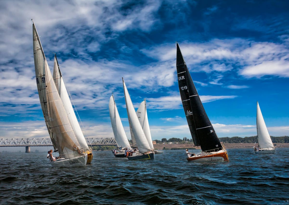 A fleet of sailboats racing through Charleston Harbor during a regatta with the city skyline in the background.