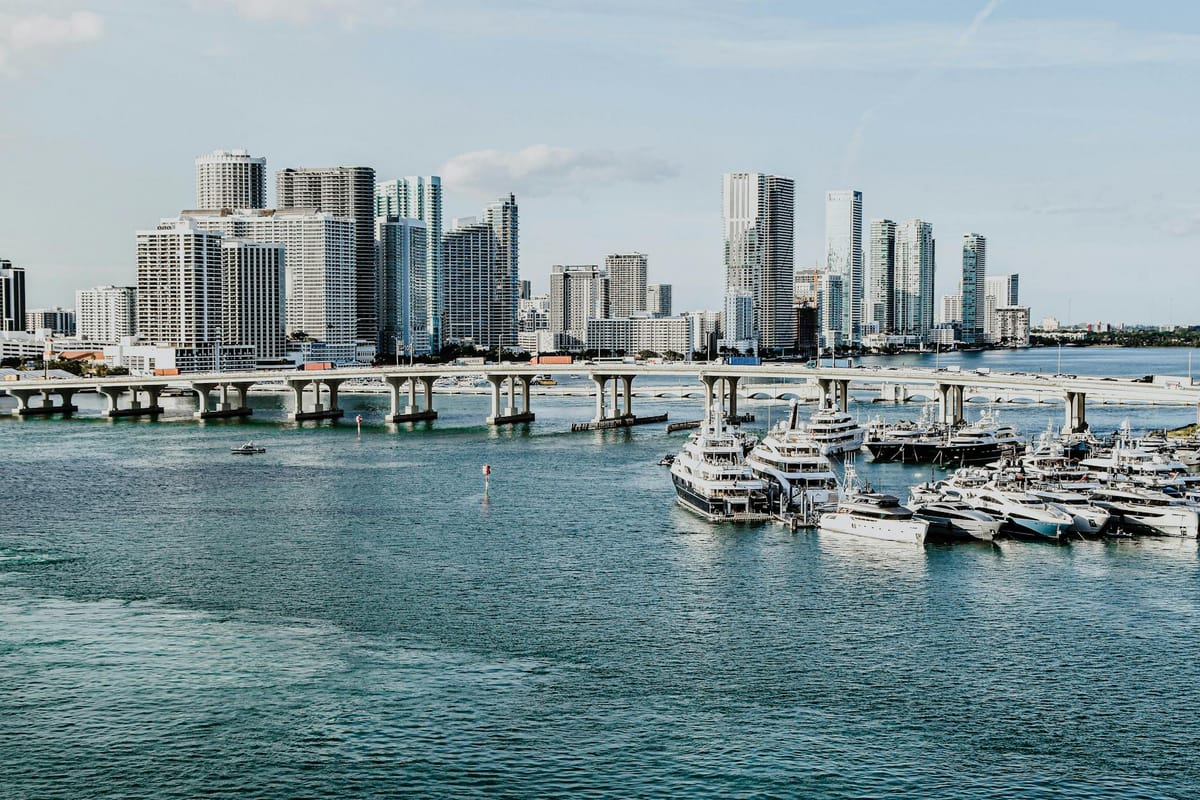 Corporate guests mingling on a yacht deck on a sunny afternoon with Biscayne Bay in the background.