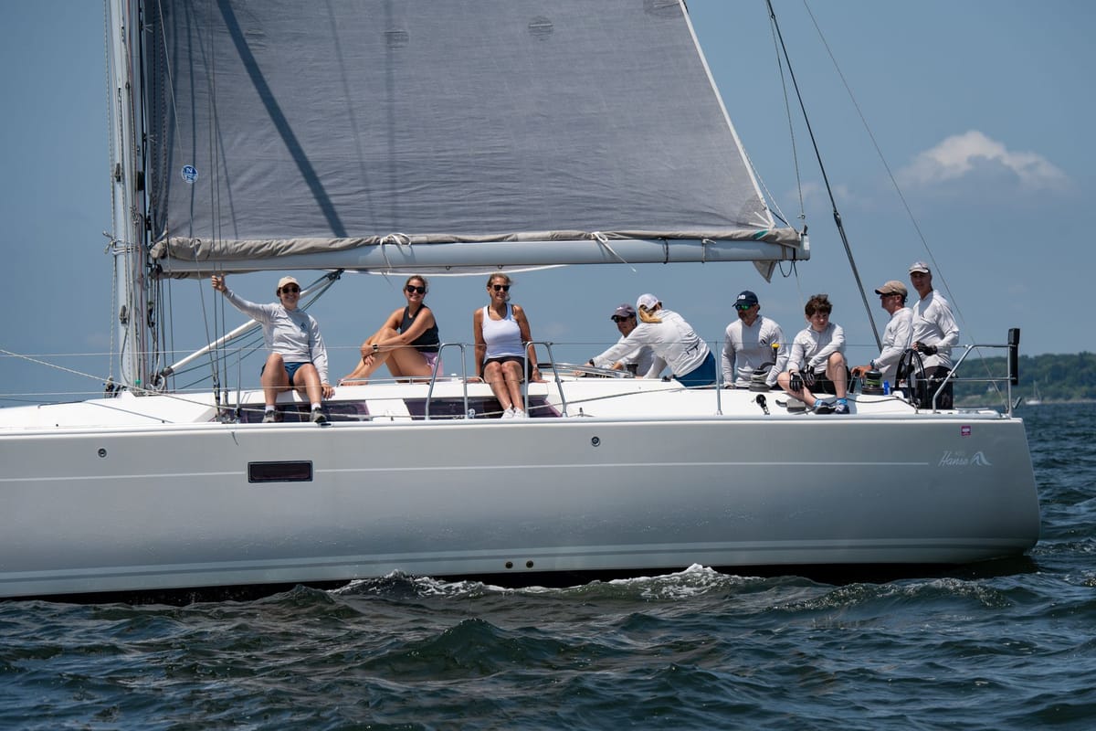 A group of guests relaxing on a private yacht deck watching a sailboat race on the water.