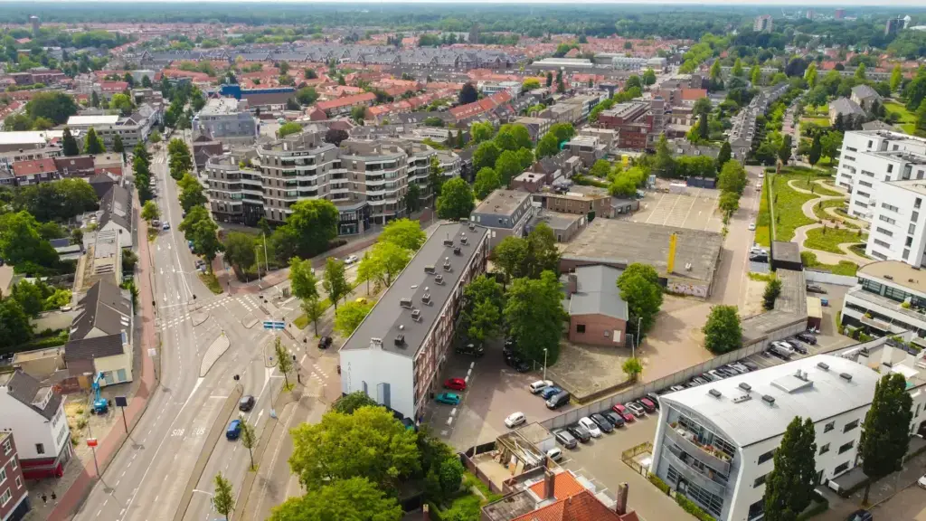 Aerial view over Eindhoven on a summer day, showing low-rise housing blocks, tree-lined streets and the city spreading out towards the horizon