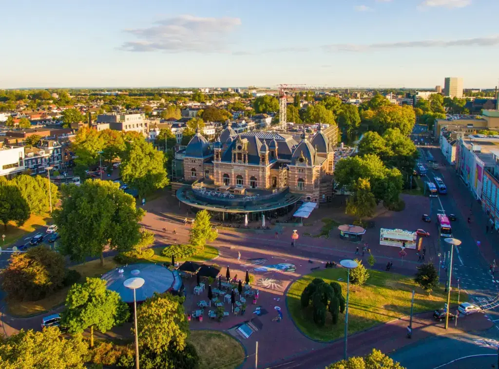 Aerial view over Arnhem at golden hour, with the Musis Sacrum concert building among trees and the city stretching to the horizon