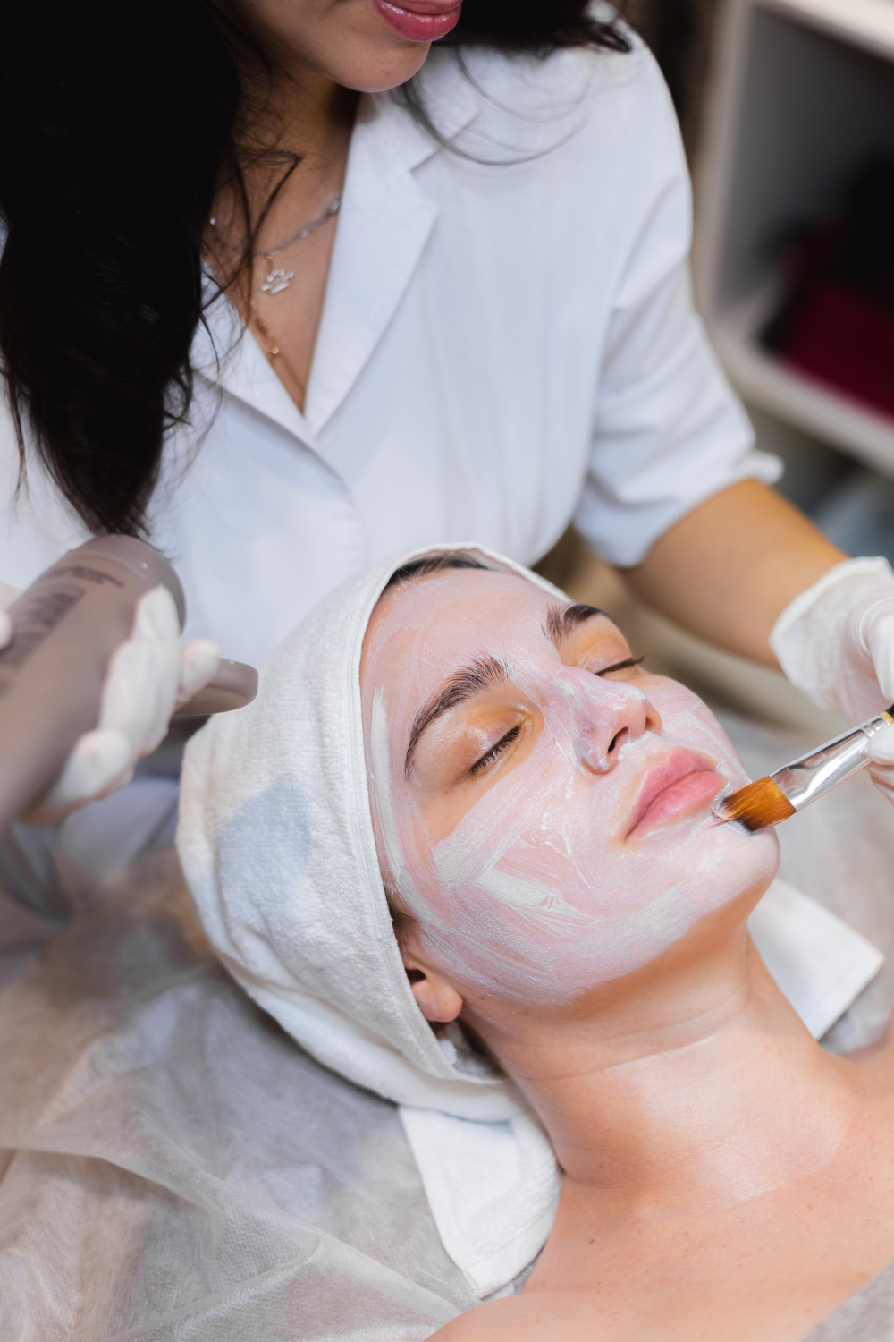 Skincare professional applying a chemical peel to a woman's face.