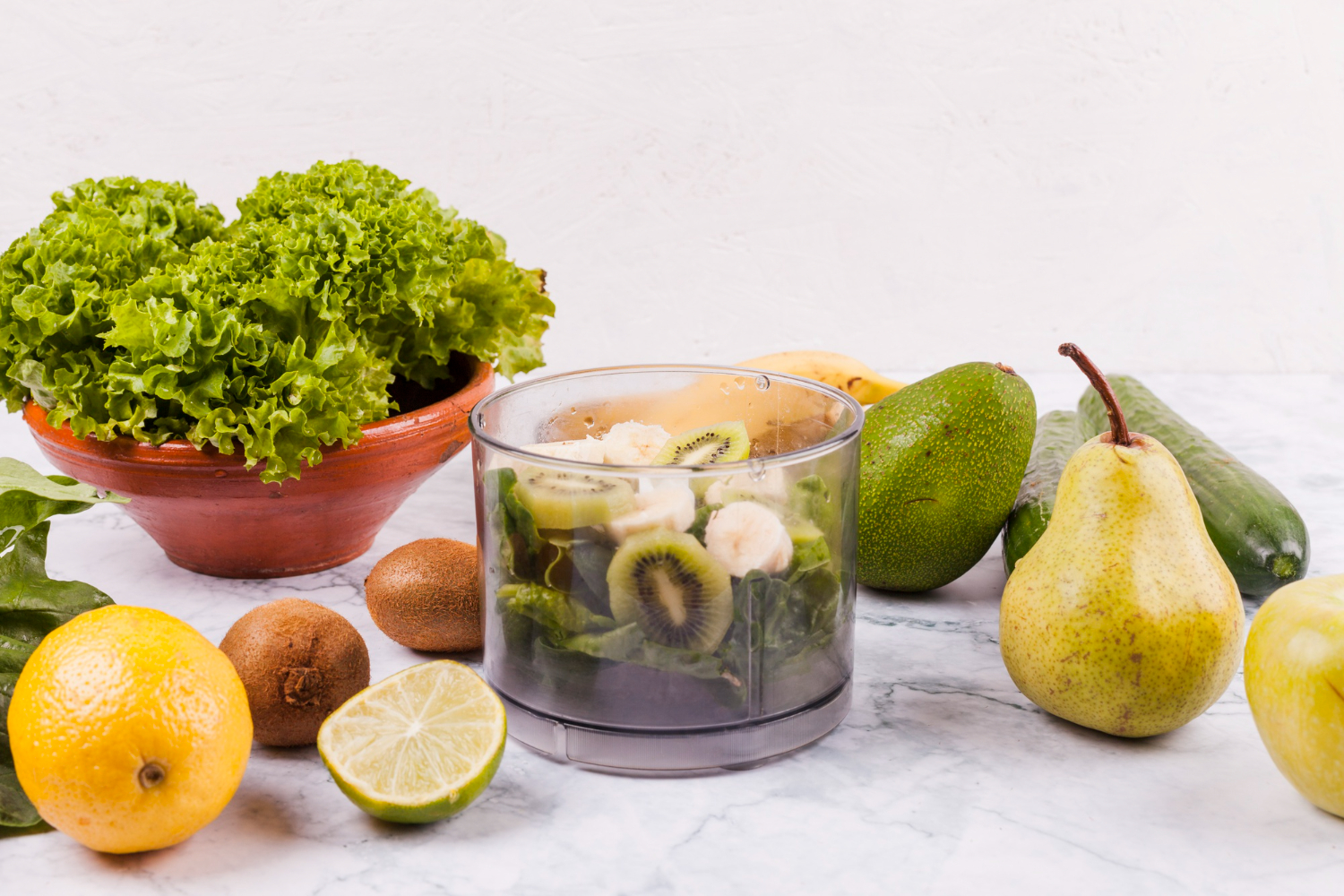 A glass of water with fresh fruits and vegetables beside it.