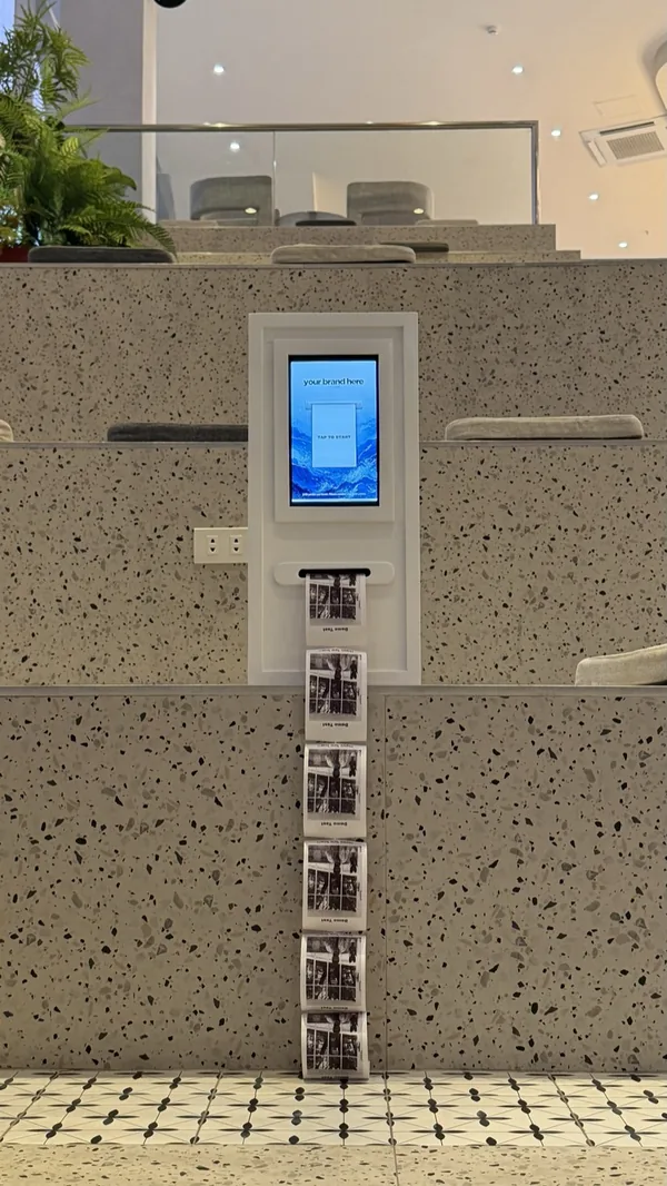 A Click2Keep booth recessed into a cafe reception counter, prints feeding out of the front slot