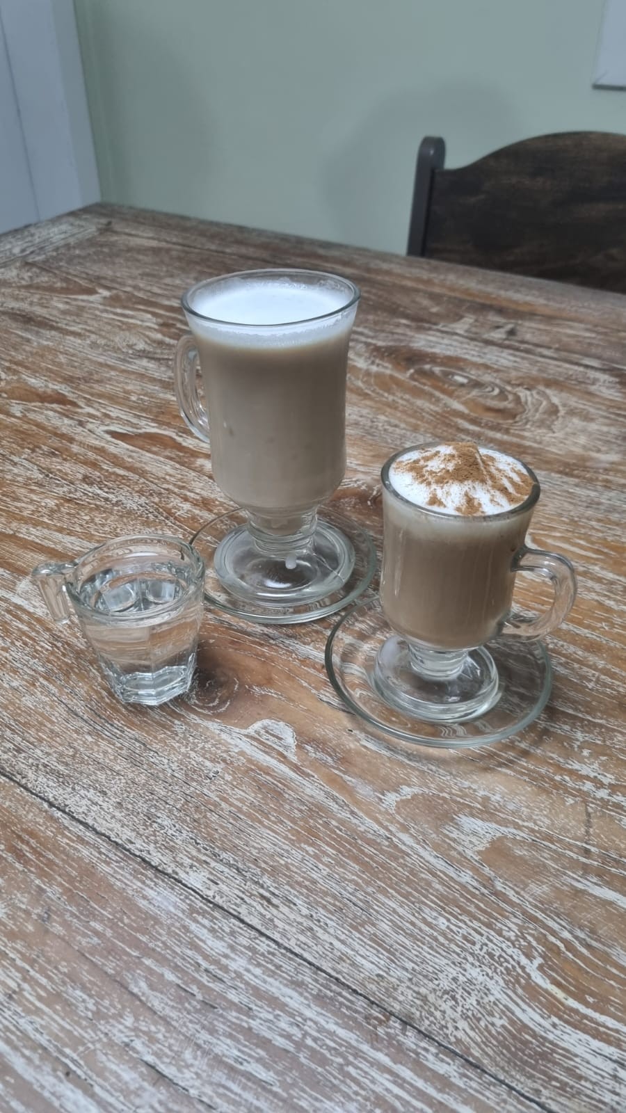 Um Latte Macchiato gelado e, ao lado, um Cappuccino com canela em pó.