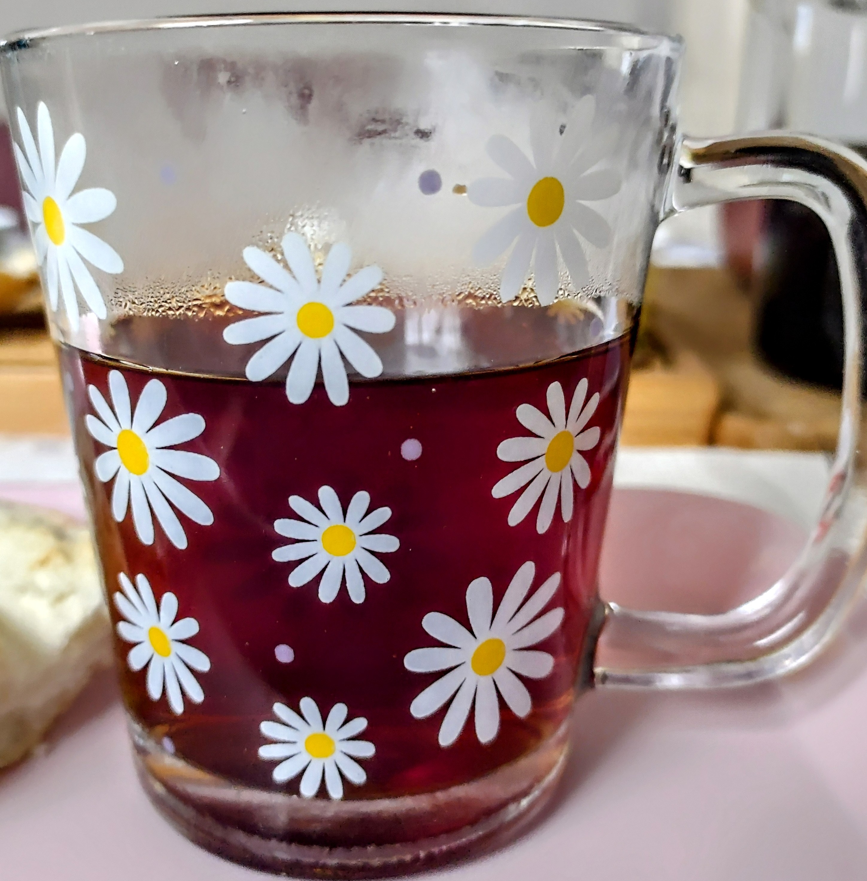 Caneca de vidro transparente com margaridas no corpo da caneca. Origem e procedência desconhecida. Na base interna da caneca, registro da palavra 