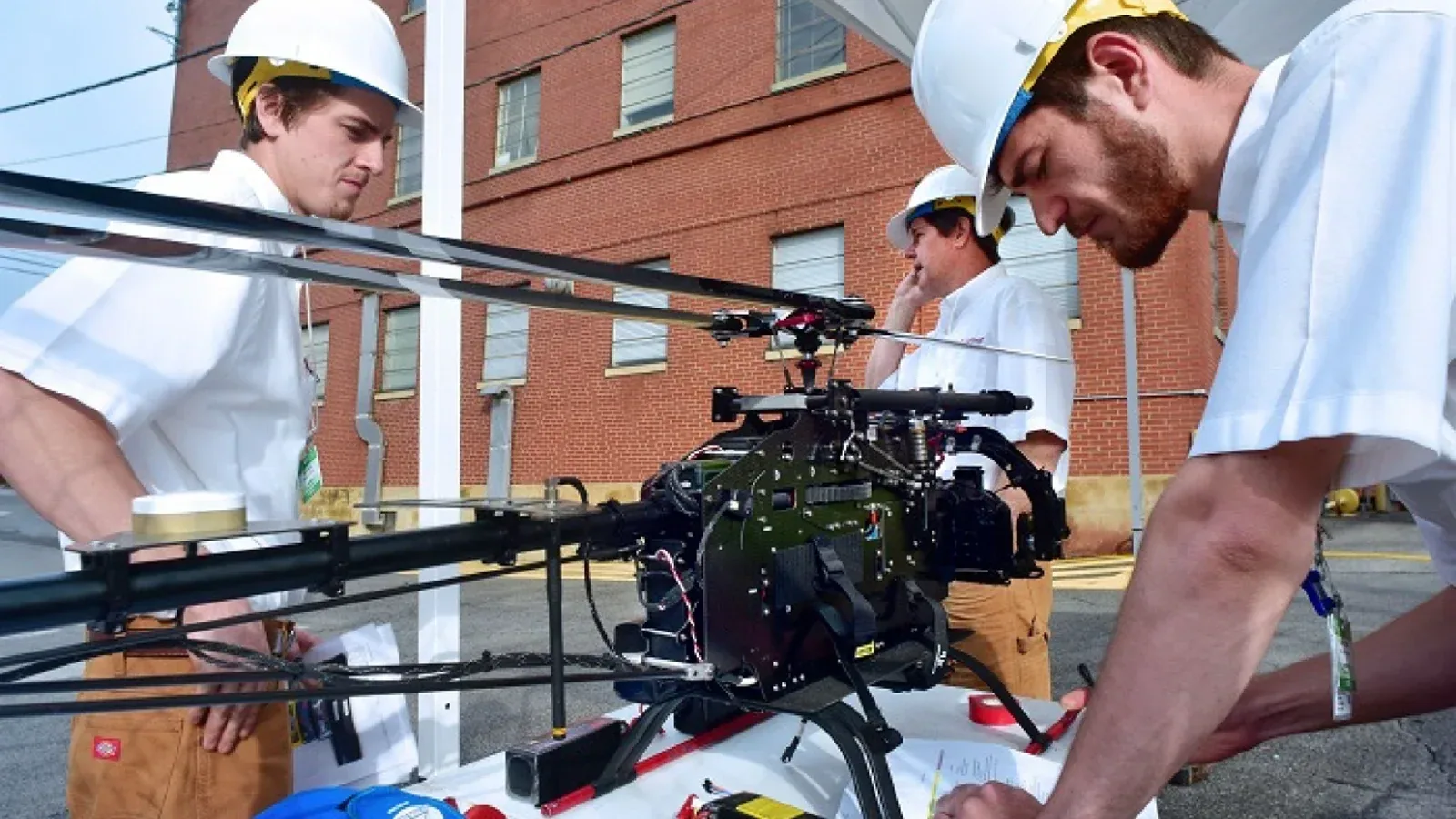 Workers in hard hats prepare a camera-carrying mini-helicopter drone for an exhaust-stack inspection at Oak Ridge.