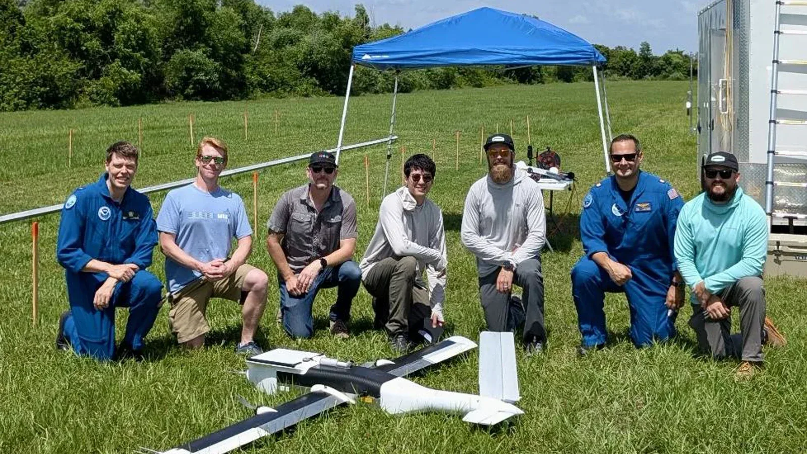NOAA and Dragoon team members kneel behind the fixed-wing Dragoon Coriolis uncrewed aircraft during a field test.