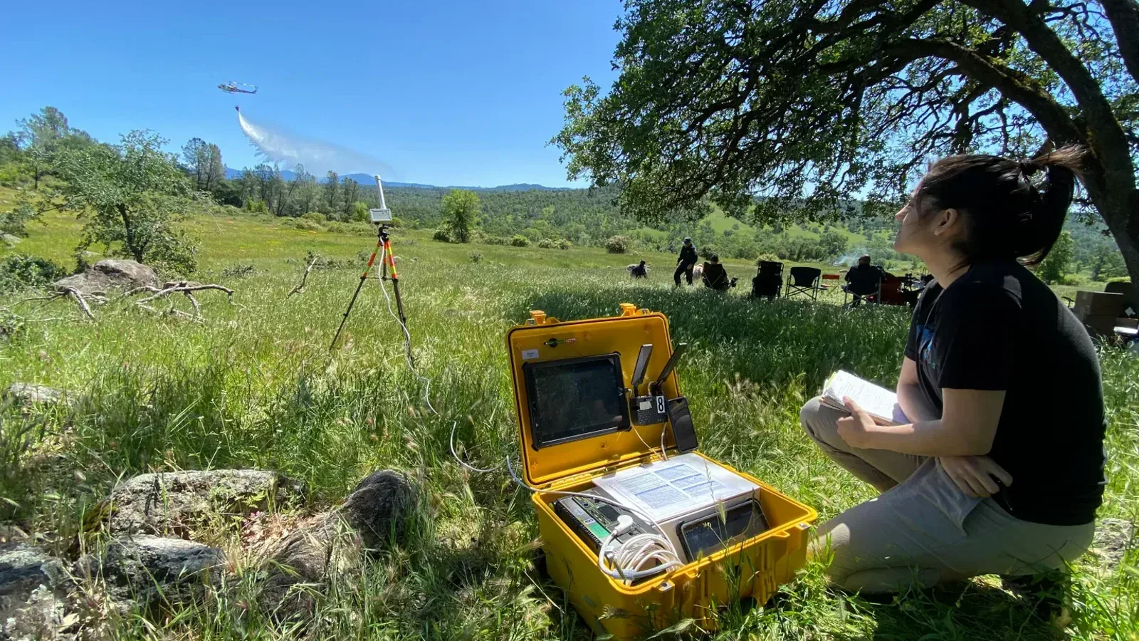 A NASA researcher tests a prototype kit for firefighting-drone operators while a helicopter performs a water drop.