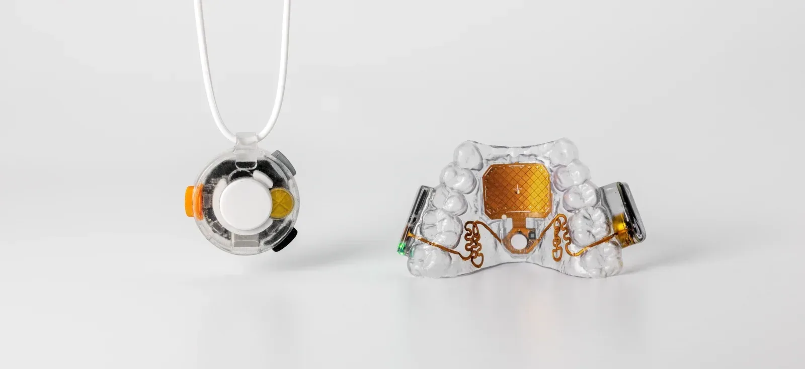 Augmental VOX pendant beside the clear MouthPad with its gold-colored touch surface.
