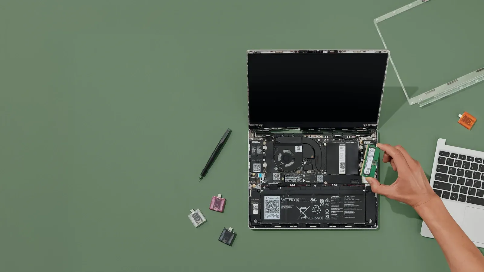 An open Framework Laptop 13 with a hand installing memory, shown as a repairable laptop example.
