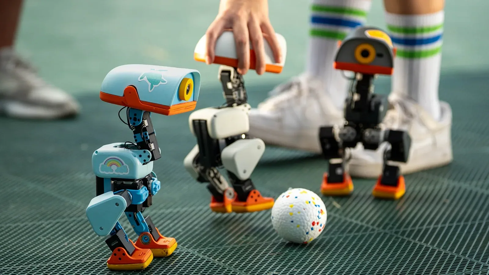 Two Microduck robots beside a ball on a turf playing field.
