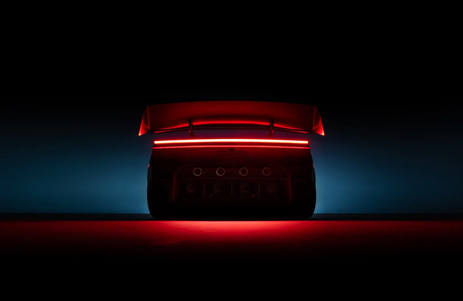 Illuminated rear light bar and raised rear wing against a dark background.