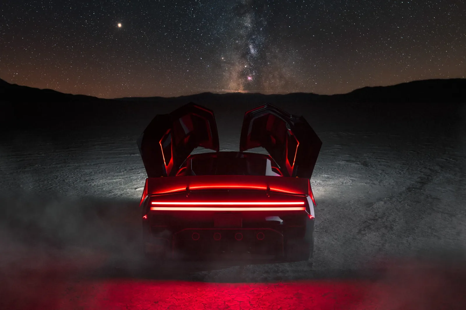 Rear view with both doors raised beneath the night sky.