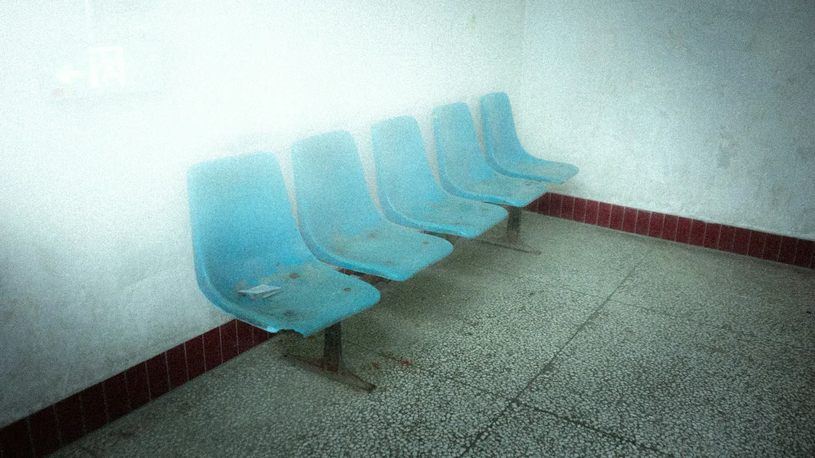 A row of empty turquoise chairs in a quiet medical waiting area