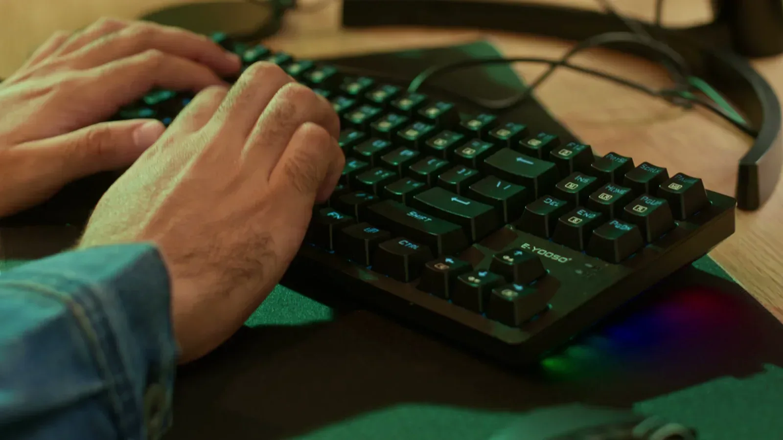Hands typing on a computer keyboard beside a mouse and headset