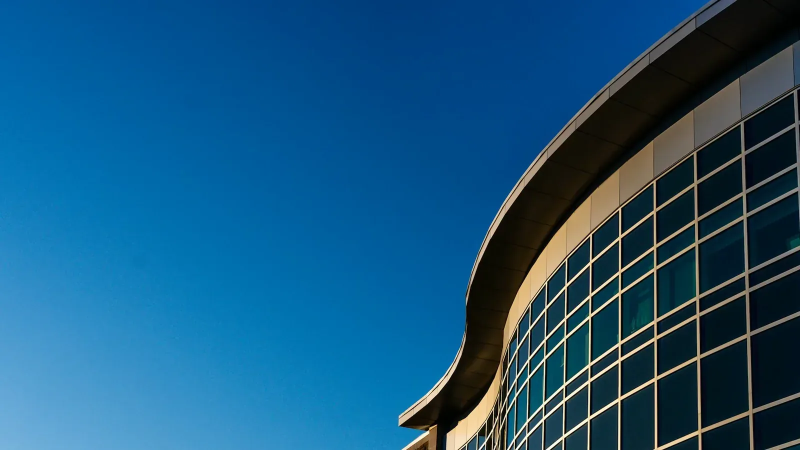 The curved glass exterior of a modern medical building under a clear blue sky