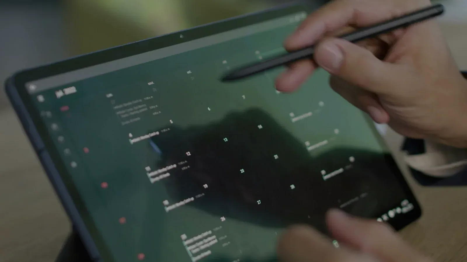 A hand using a stylus on a calendar displayed on a tablet