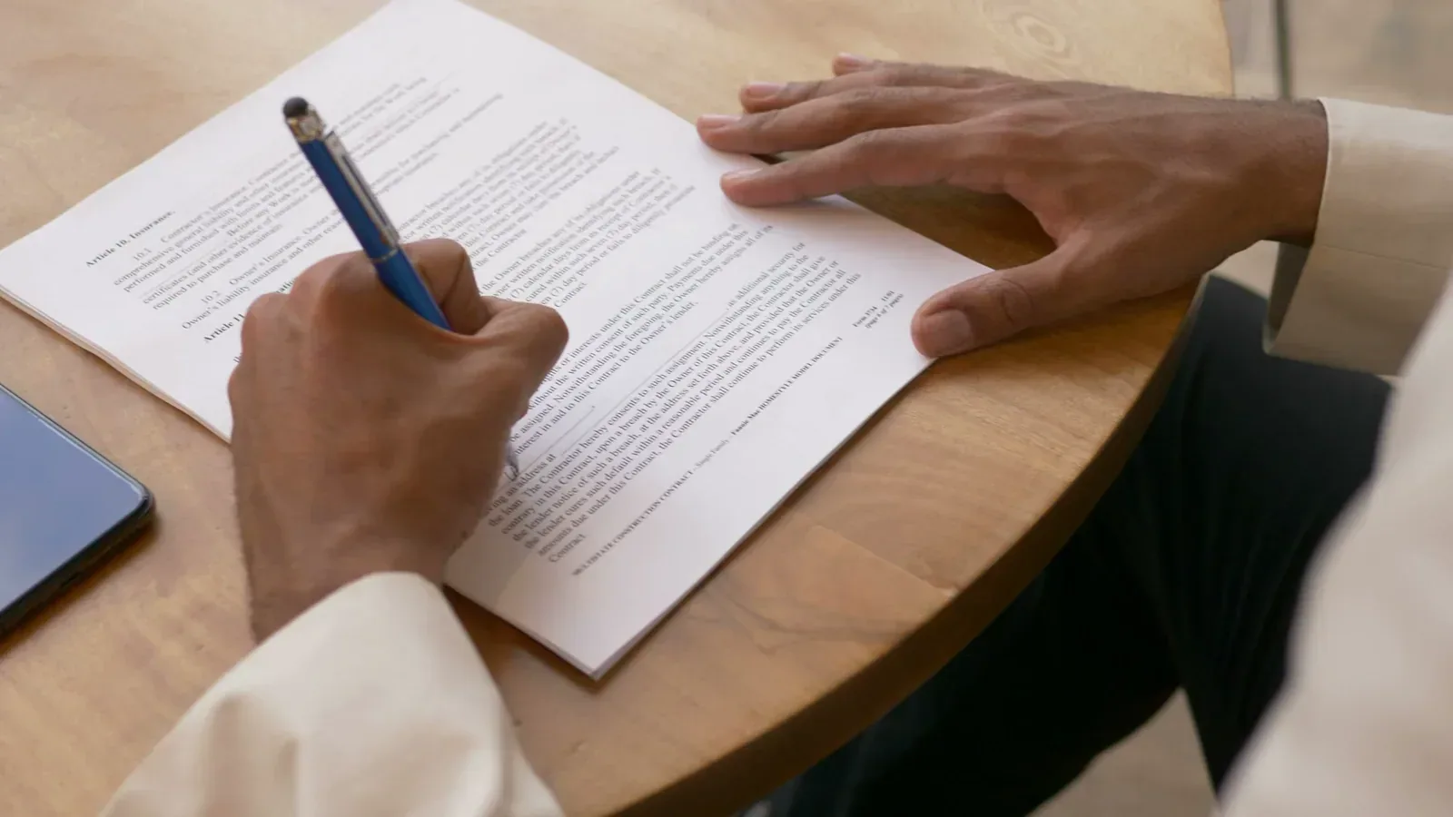 Hands signing a generic printed contract at a wooden table