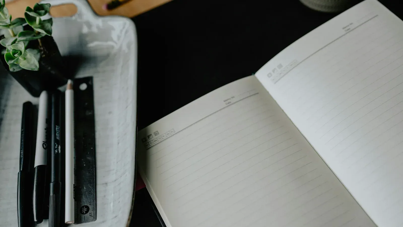 An open notebook and pens arranged on a dark desktop