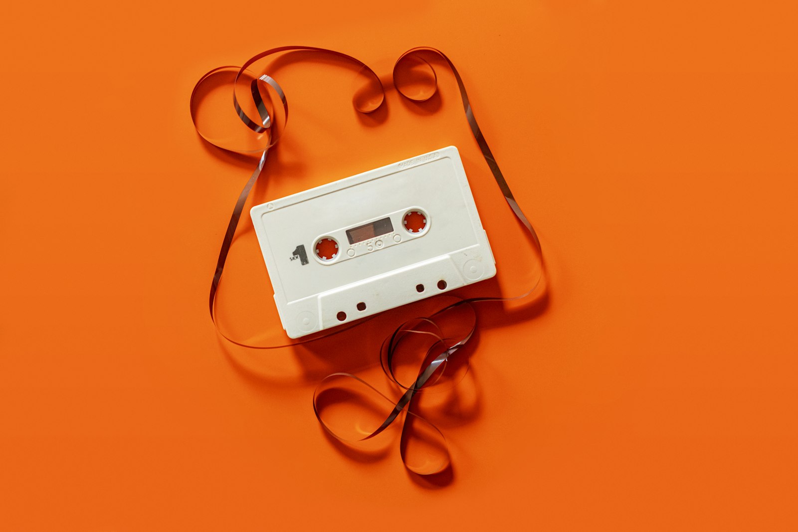 A white cassette tape on an orange surface, tape spilled in loose loops