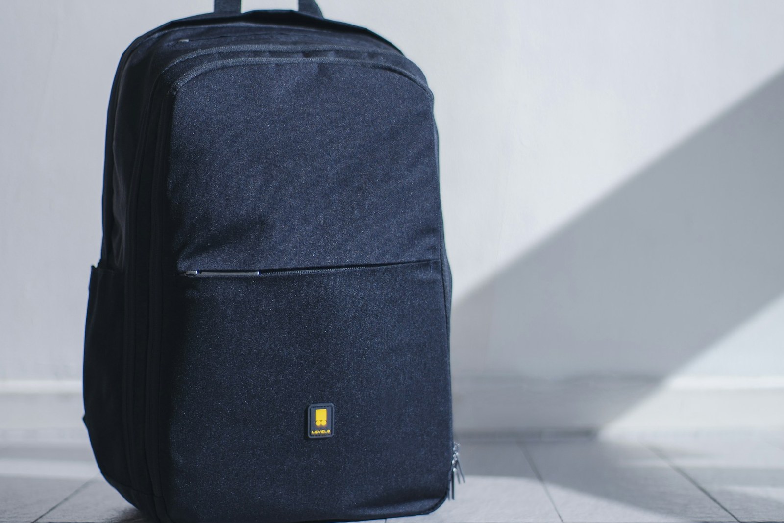 A black travel backpack standing upright on a light wood floor